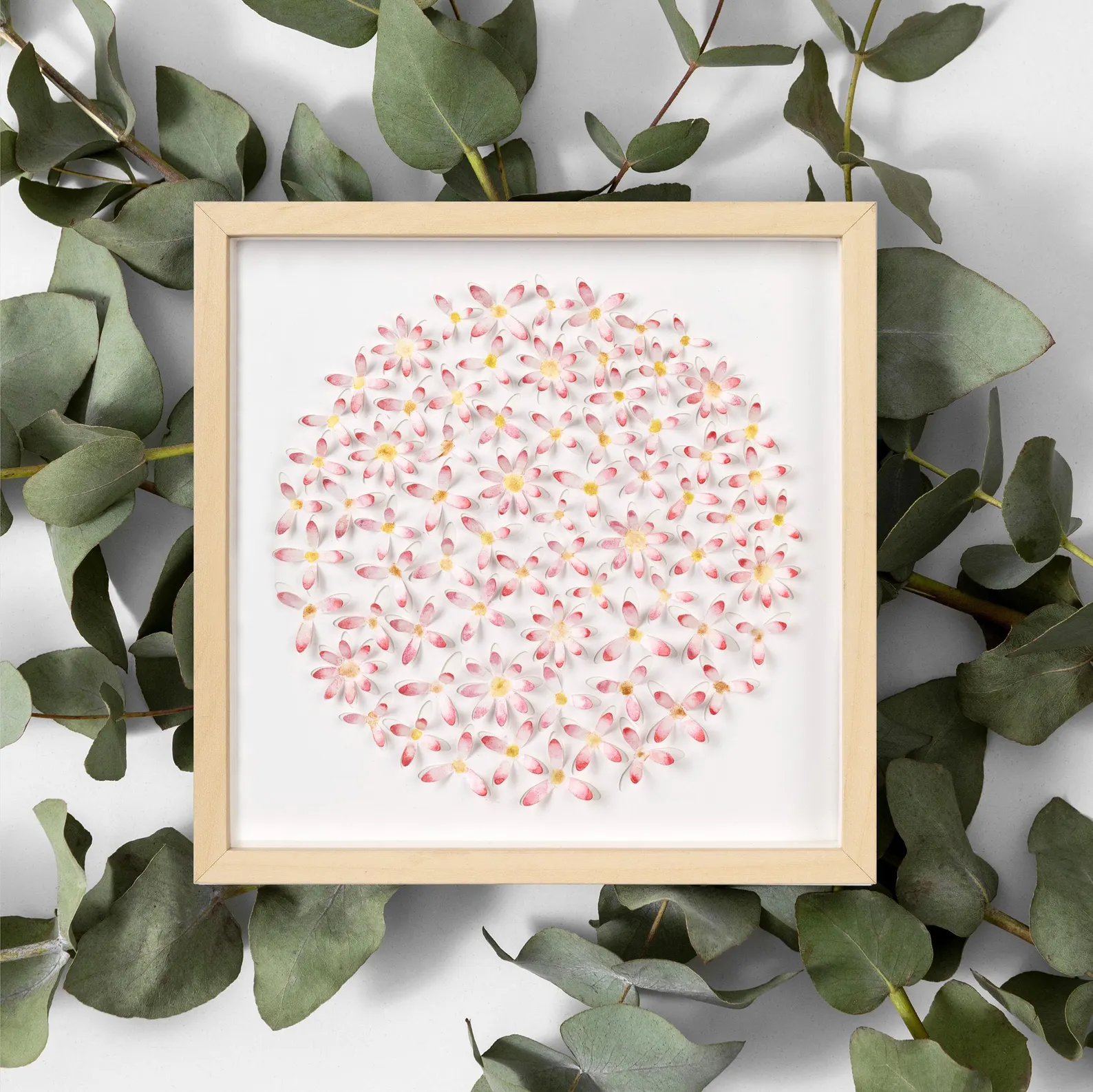 Pink daisy circle 3D watercolor wall art in a light wood frame styled with eucalyptus leaves